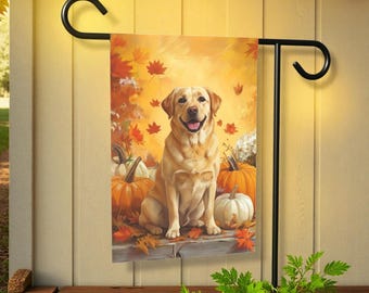 Pode incluir: Uma bandeira de jardim decorativa com um Labrador Retriever amarelo sentado entre abóboras e folhas de outono. O fundo é um tom dourado quente, com folhas caindo que adicionam ao tema do outono. A bandeira é exibida em um suporte de metal preto.