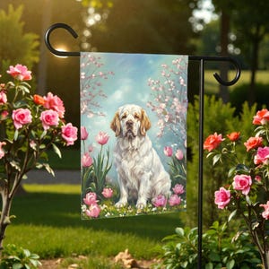 May include: A garden flag featuring a seated white dog with tan ears and a serene expression. The dog is surrounded by pink tulips and flowering branches against a light blue sky. The flag is displayed on a black metal stand.