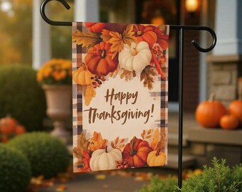 Könnte beinhalten: Eine Gartenflagge auf einem schwarzen Metallständer. Die Flagge zeigt einen karierten Rand und ein zentrales Design aus Kürbissen, Blättern und dem Text "Happy Thanksgiving!" in einer dekorativen Schriftart. Die Kürbisse sind in Orange- und Weißtönen gehalten.