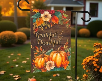 Può includere: Una bandiera da giardino decorativa a tema autunnale, con zucche, fiori e la scritta "Grateful & Thankful" su uno sfondo di legno. La bandiera è esposta su un supporto in metallo nero, ideale per l'arredamento esterno autunnale.