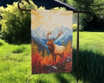May include: A garden flag depicting an elk with large antlers, set against a backdrop of mountains and a colorful forest. The artwork uses warm tones of orange, red, and yellow, creating a vibrant outdoor scene.