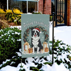 May include: A garden flag featuring a black and white Border Collie wearing a Santa hat, surrounded by a Christmas wreath and gifts. The flag reads "Merry Christmas!" in white script against a light blue background. The flag is displayed outdoors in a snowy setting.