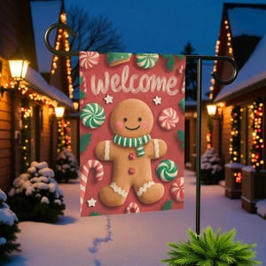 May include: A red garden flag with a gingerbread man design. The flag says "Welcome" and features a gingerbread man with a green and white scarf, surrounded by candies and stars. The flag is displayed outdoors.