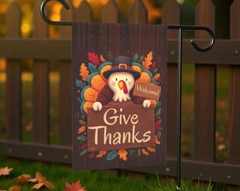 Può includere: Una bandiera da giardino del Ringraziamento con un tacchino dei cartoni animati con un cappello da pellegrino e un cartello con la scritta "Give Thanks". La bandiera ha uno sfondo in legno con foglie d'autunno colorate e un cartello "Welcome".