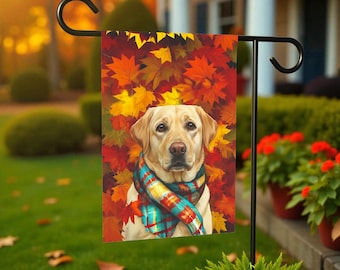 Pode incluir: Uma bandeira de jardim com um Labrador Retriever amarelo usando um cachecol xadrez, em um fundo de folhas de outono em tons de vermelho, laranja e amarelo. A bandeira é exibida em um suporte de metal preto, ideal para decoração ao ar livre.