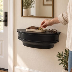 May include: A semi-circular black wall-mounted console shelf with tiered molding details. On the shelf sits a rectangular beige tray containing a brown leather wallet and a set of metal keys, alongside a pair of dark-rimmed eyeglasses.