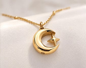 Könnte beinhalten: Eine goldfarbene Anhängerkette in Form eines Halbmondes mit einem kleinen vierzackigen Stern in der Wölbung. Der Anhänger hängt an einer zarten goldfarbenen Kette und weist eine kleine Schraube an der Seite des Mondes auf.