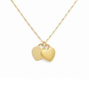 Pu&ograve; includere: Una collana color oro caratterizzata da una sottile catena ritorta e due ciondoli lisci a forma di cuore che pendono affiancati. I ciondoli hanno una superficie lucida e riflettente e sono fissati alla catena tramite piccoli anellini.