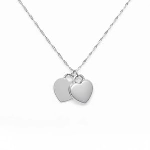 Pu&ograve; includere: Una collana color argento con una sottile catenina intrecciata e due ciondoli a forma di cuore, lisci e lucidi, che pendono affiancati. La superficie metallica &egrave; riflettente e semplice, caratterizzata da un design essenziale senza incisioni.