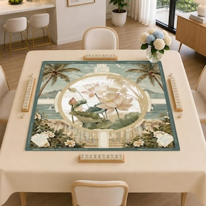 Puede incluir: Un tapete de mahjong cuadrado con un dise&ntilde;o circular central de flores de loto rosas y hojas verdes. El borde muestra palmeras, un paisaje costero y una balaustrada de piedra. El texto DRACO'S COLLECTION est&aacute; impreso en el borde superior.