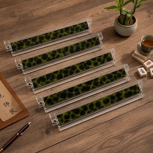 May include: Five rectangular clear acrylic display stands arranged in a diagonal row. Each stand features a long, narrow insert with a dark green and black mottled, organic pattern resembling a cell structure or animal print texture.