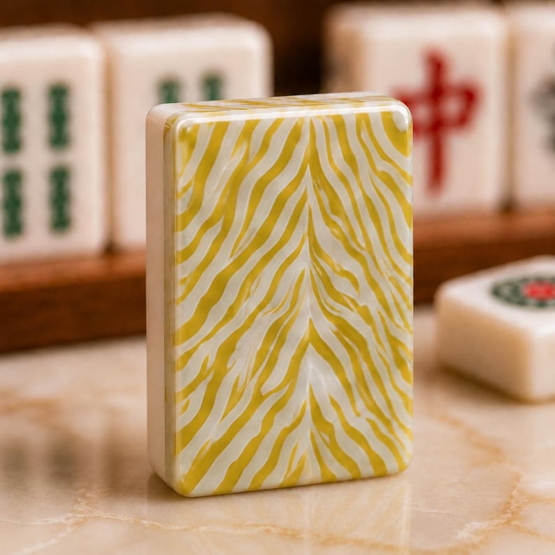 May include: A rectangular mahjong tile standing upright, featuring a glossy, marbled yellow and white zebra-stripe pattern on its back. The tile has smooth, rounded edges and a solid white side profile, contrasting with other tiles in the background.