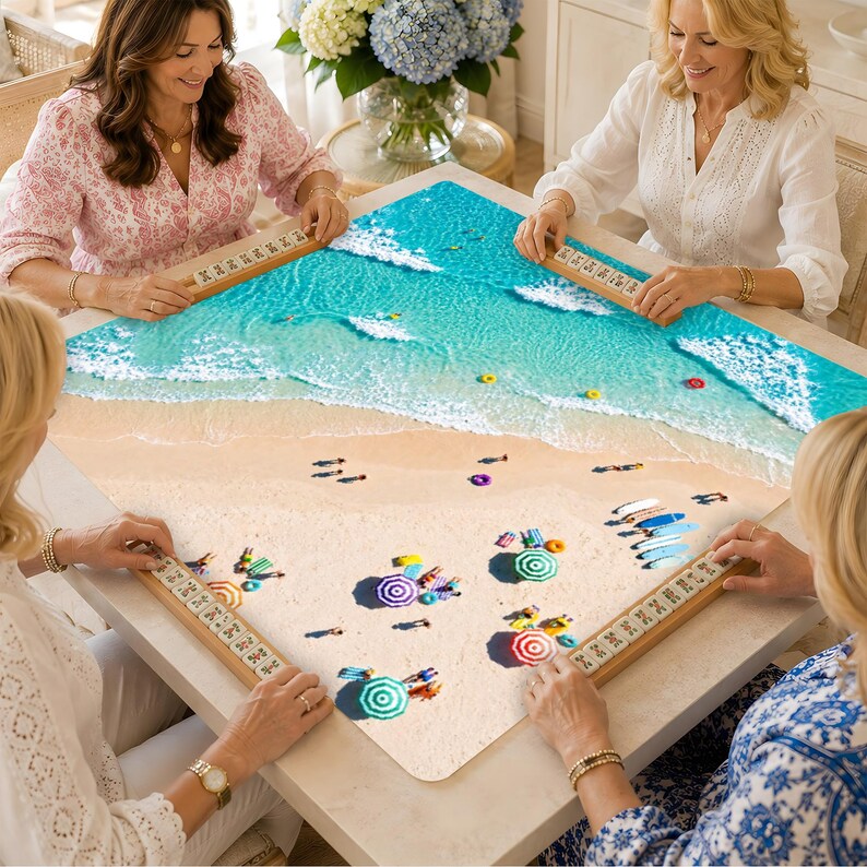 May include: A square board game featuring a high-angle view of a sandy beach with turquoise ocean waves, colorful umbrellas, and small figures. Four wooden tile racks are positioned along the edges of the board, each holding numbered game tiles.