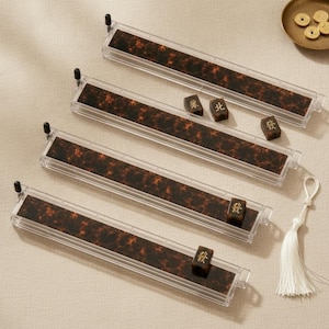 May include: Four rectangular mahjong tile racks made of clear acrylic with a dark brown tortoiseshell pattern insert. Each rack features a small black peg at one end and is accompanied by three individual mahjong tiles with gold characters.