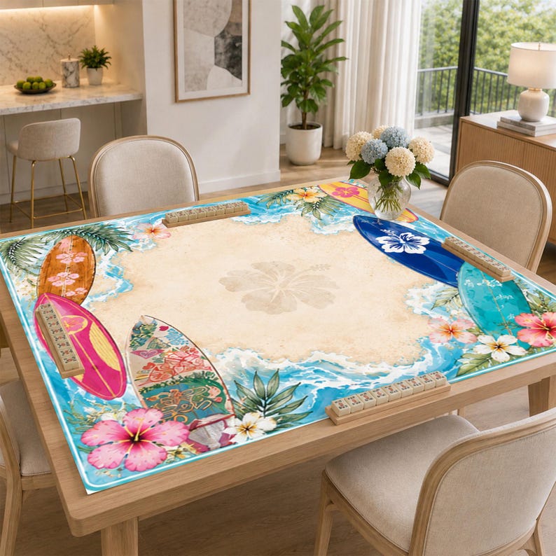 May include: A square mahjong table mat featuring a beach-themed design with a sandy center, blue ocean waves, tropical hibiscus flowers, and colorful surfboards. Four wooden tile racks are positioned along the edges of the mat.