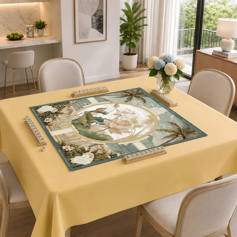 Puede incluir: Una alfombrilla de mahjong cuadrada sobre un mantel amarillo claro. La alfombrilla presenta una ilustraci&oacute;n circular central de flores de loto rodeadas de palmeras y columnas arquitect&oacute;nicas. Cuatro soportes de madera est&aacute;n en los bordes.