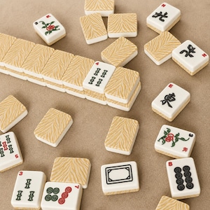 May include: A collection of mahjong tiles featuring a mix of white tiles with black, red, and green ink illustrations of characters, bamboo, and circles, alongside tiles with a tan and white tiger-stripe pattern on the reverse side.