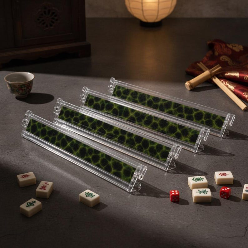 May include: Four clear plastic mahjong tile racks featuring a dark green and black honeycomb pattern insert. The set is accompanied by several white mahjong tiles with red and green characters, along with two small red dice on a dark surface.