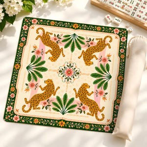 May include: A square game mat featuring a cream-colored center with four illustrated leopards, green palm-like leaves, and pink flowers. The border is dark green with orange and pink floral patterns. A matching fabric storage bag is included.