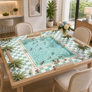 May include: A square table cover featuring a printed swimming pool scene with light blue water, swimmers, and palm trees, surrounded by a white and teal checkered border. Four wooden tile racks are placed along the edges of the table surface.