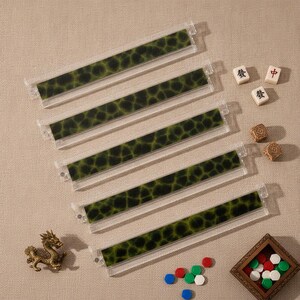 May include: Five clear acrylic mahjong tile racks featuring a dark green and black mottled pattern. The set includes three small white mahjong tiles with black and red characters, two brown textured dice, a gold dragon figurine, and small tokens.