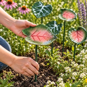 May include: A set of garden stakes featuring glossy, heart-shaped leaves in shades of green and pink with prominent red veins. Each leaf is attached to a thin, dark green metal rod, designed to be inserted into soil for outdoor plant decoration.