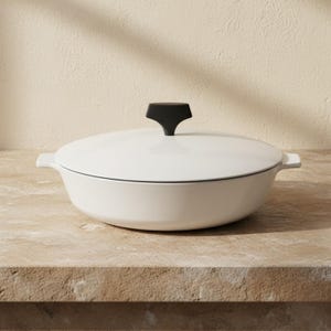 May include: A white shallow cooking pan with a matching lid and a black T-shaped handle. The pan features two integrated side handles and a smooth, rounded base, presenting a clean and functional design for stovetop cooking tasks.