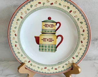 Puede incluir: Plato de cerámica decorativo con un diseño de cafetera apilada. El plato tiene un centro color crema con una ilustración detallada de una cafetera amarilla y verde. El borde tiene un borde estampado con motivos de tazas de café y un diseño a cuadros rojo y negro.