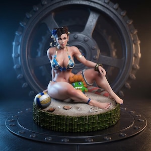 Pode incluir: Uma figura colecionável de uma personagem com cabelo escuro em coques, vestindo um biquíni azul e dourado, sentada numa base arenosa com uma bola de voleibol, uma pequena criatura verde e uma borda de bambu, perante um grande engrenagem escura.