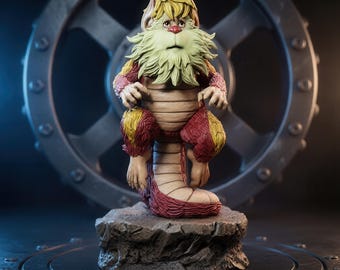 May include: A fantasy creature figurine with blonde hair, a light green beard, and a red nose. The creature has a tan, segmented torso and tail, with red and yellow fur on its limbs. It sits on a textured, dark gray rock-like base.