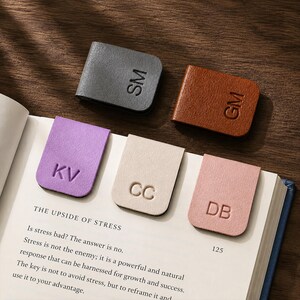 May include: Five rectangular magnetic bookmarks in gray, brown, purple, cream, and pink. Each bookmark features two embossed capital letters: SM, GM, KV, CC, and DB. Three bookmarks are clipped onto the pages of an open book titled The Upside of Stress.