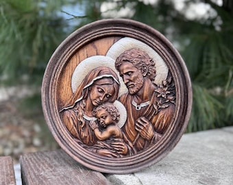 May include: A round, wooden relief carving depicting the Holy Family. The artwork features Joseph, Mary, and the infant Jesus, with halos. The carving is in shades of brown and is set within a circular frame.
