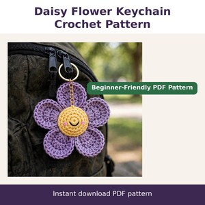 May include: A crochet daisy flower keychain with purple petals and a yellow centre featuring a stitched smiley face. The text reads Daisy Flower Keychain Crochet Pattern, Beginner-Friendly PDF Pattern, and Instant download PDF pattern.