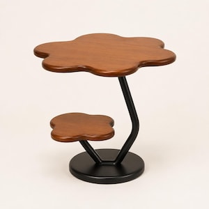 May include: A two-tiered side table featuring a large flower-shaped wooden top and a smaller flower-shaped wooden shelf. The structure is supported by a black metal frame that connects to a solid, circular black metal base on the floor.