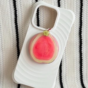 May include: White phone case featuring a pink and red fruit design, possibly a guava, with a green stem. The case has a ridged texture and a cutout for the camera. The fruit design has a clear, glossy finish.
