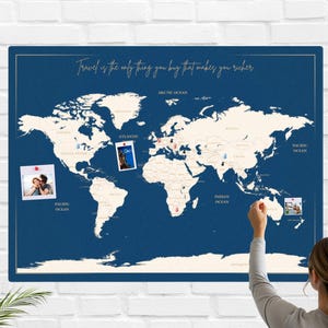May include: A navy blue world map with a gold border and the quote "Travel is the only thing you buy that makes you richer." The map has pins and photos attached. The map is mounted on a white brick wall.