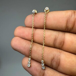 Puede incluir: Un par de pendientes colgantes de oro con un diseño de cadena fina. Cada pendiente tiene una piedra redonda engastada en bisel en el poste superior y tres piedras redondas más pequeñas engastadas en el extremo de la cadena dorada.