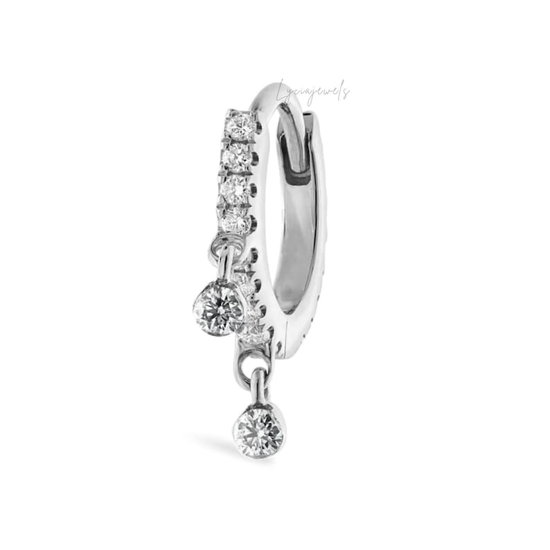 May include: A silver hoop earring with a row of small, clear stones along the front. Two clear, round stones dangle from the bottom of the earring. The earring is set against a white background.