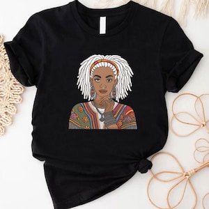 Könnte beinhalten: Schwarzes T-Shirt mit einer grafischen Illustration einer Frau mit weißen Dreadlocks, einem roten Stirnband und Schmuck. Die Frau wird mit nachdenklichem Ausdruck dargestellt und trägt ein gemustertes Oberteil. Das Design ist eine grafische Darstellung eines kulturellen Themas.