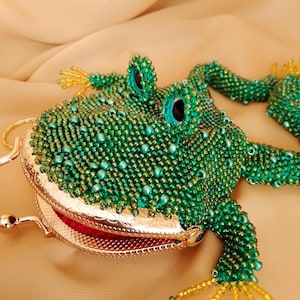 May include: A beaded frog-shaped coin purse in shades of green, with gold accents on the feet and clasp. The frog's eyes are a striking turquoise color. The purse has a red interior and a metal clasp.