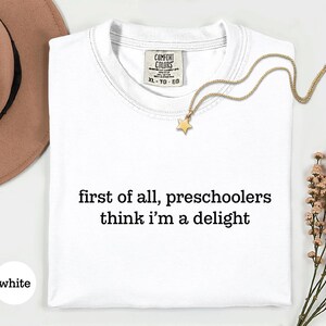 May include: A white short-sleeved t-shirt with the black text 'first of all, preschoolers think i'm a delight' printed on the front. The shirt features a Comfort Colors brand label at the inner neckline indicating size XL, TG, EG.