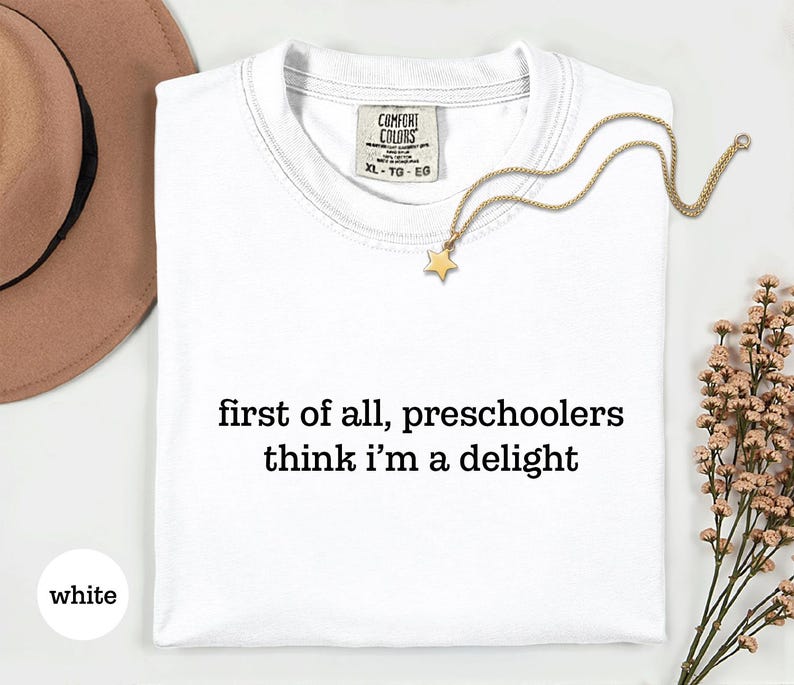 May include: A white short-sleeved t-shirt with the black text 'first of all, preschoolers think i'm a delight' printed on the front. The shirt features a Comfort Colors brand label at the inner neckline indicating size XL, TG, EG.
