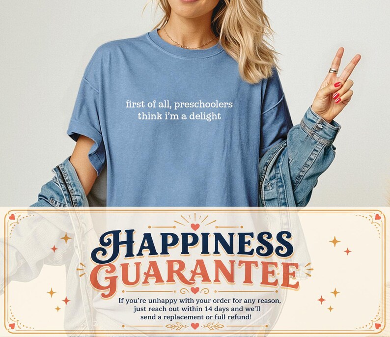 May include: A blue short-sleeved t-shirt featuring the white text "first of all, preschoolers think i'm a delight" printed on the chest. The shirt has a crew neckline and a relaxed fit, worn layered under a blue denim jacket.