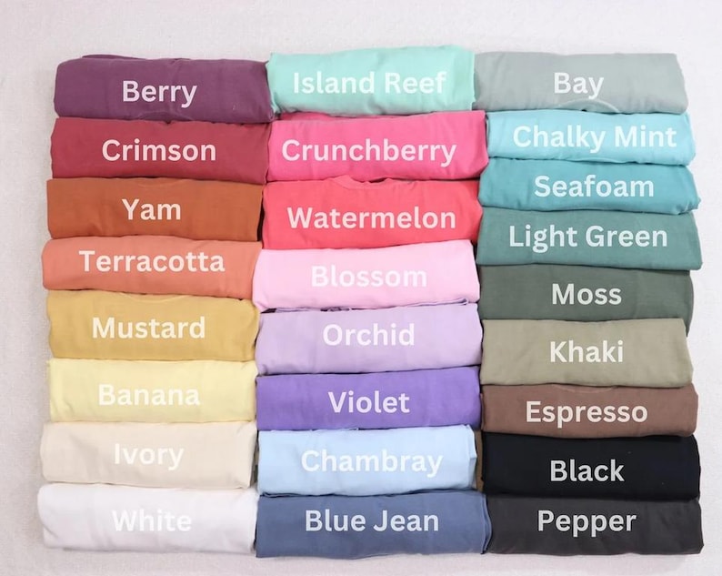Peut inclure: Une collection de t-shirts pli&eacute;s dispos&eacute;s en grille, chacun &eacute;tiquet&eacute; avec son nom de couleur : Berry, Crimson, Yam, Terracotta, Mustard, Banana, Ivory, White, Island Reef, Crunchberry, Watermelon, Blossom, Orchid, Violet, Chambray, Blue Jean, Bay, Chalky Mint, Seafoam, Light Green, Moss, Khaki, Espresso, Black et Pepper.