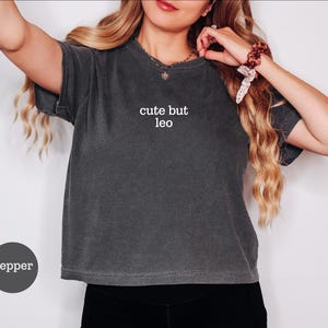 Peut inclure: Un t-shirt &agrave; manches courtes gris anthracite avec une finition d&eacute;lav&eacute;e vintage. Le centre de la poitrine pr&eacute;sente le texte blanc "cute but leo" imprim&eacute; dans une police sans empattement simple. Le v&ecirc;tement a un col rond et une coupe ample.