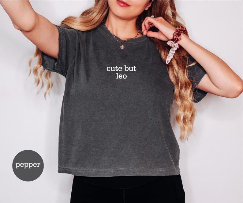 Peut inclure: Un t-shirt &agrave; manches courtes gris anthracite avec une finition d&eacute;lav&eacute;e vintage. Le centre de la poitrine pr&eacute;sente le texte blanc "cute but leo" imprim&eacute; dans une police sans empattement simple. Le v&ecirc;tement a un col rond et une coupe ample.