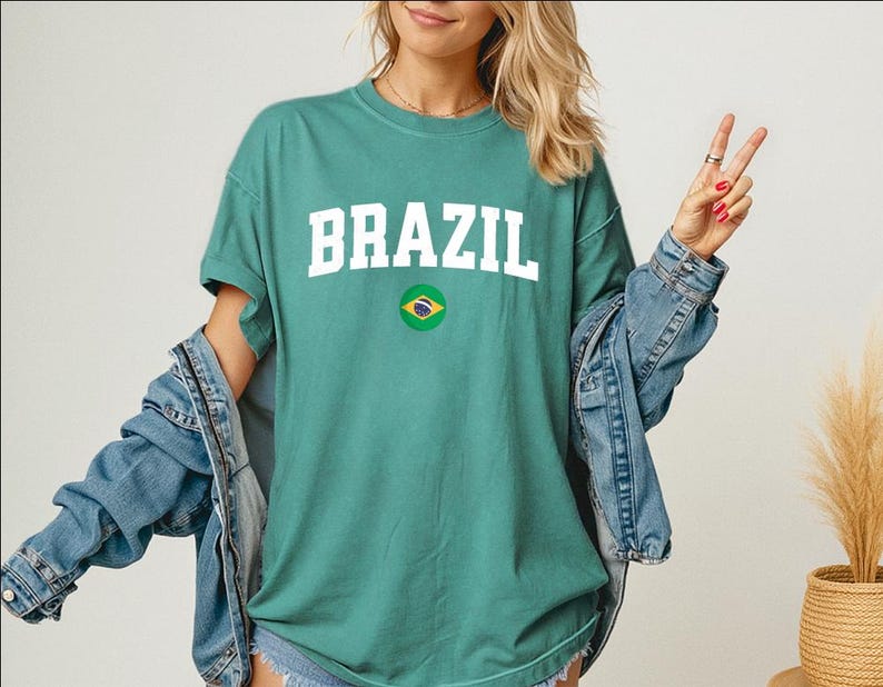 May include: A teal t-shirt with the word "BRAZIL" in white block letters and a small Brazilian flag emblem. The shirt is paired with a denim jacket.