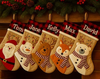 Pode incluir: Cinco meias de Natal penduradas numa lareira, cada uma com um nome bordado na bainha. As meias apresentam desenhos festivos: Pai Natal, um boneco de neve, um urso, uma raposa e um urso polar, todos com cachecóis. Uma grinalda de vegetação e bagas adorna a lareira.