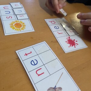 May include: Three rectangular educational cards featuring word-building activities. One card shows a sun illustration with the word sun, another shows a red paint splash with the word red, and the third shows a net illustration with the word net.