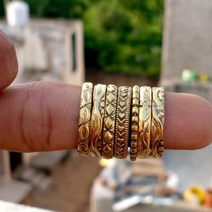Puede incluir: Una colección de ocho anillos dorados con intrincados diseños en relieve. Los anillos presentan varios patrones, incluyendo motivos florales, geométricos y de corazón. Los anillos se muestran en un dedo, mostrando su detallada artesanía.